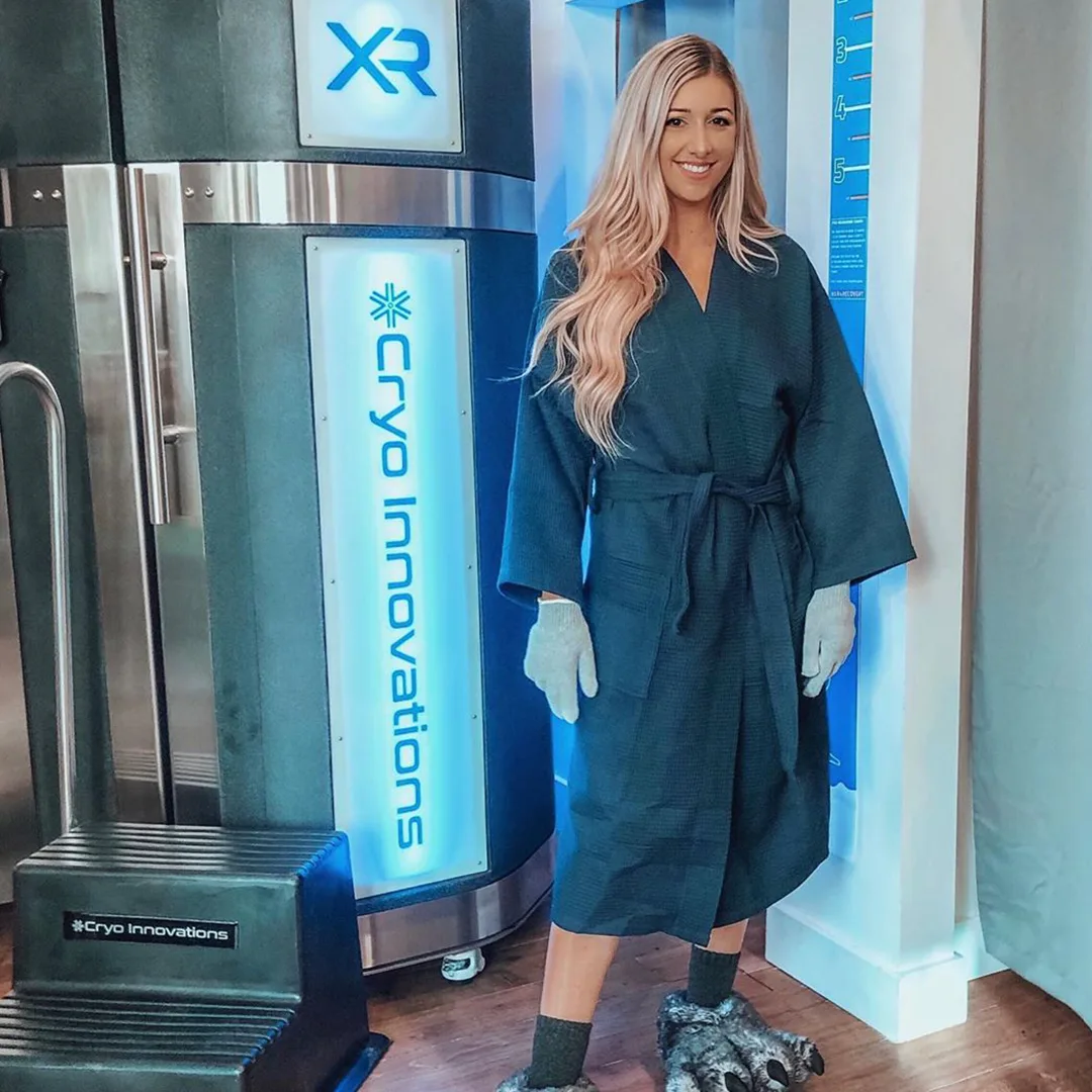 Guest in a robe, gloves and booties beside an XR chamber, ready for a session
